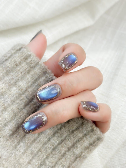 Hand with Square shaped grey-blue cat eye press-on nails with metallic shimmer and gold foil border accents