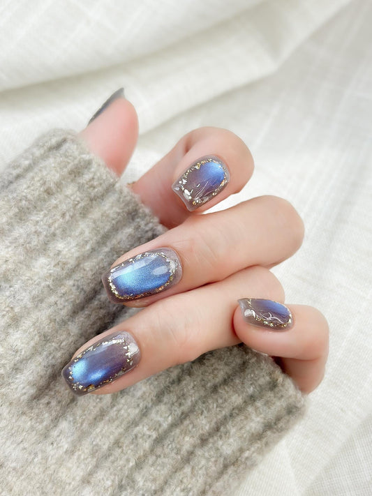 Hand with Square shaped grey-blue cat eye press-on nails with metallic shimmer and gold foil border accents