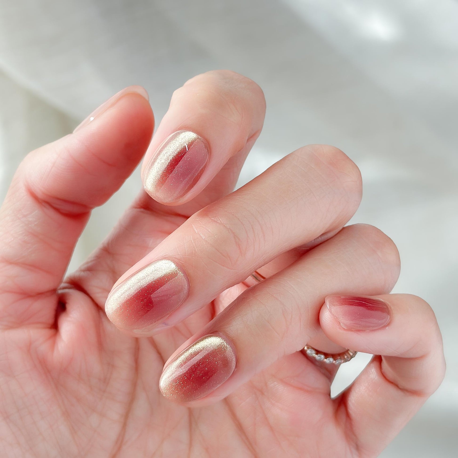 Hand with short Coral peach cat-eye press-on nails with a soft gold shimmer gradient. Short oval luxury reusable press-on