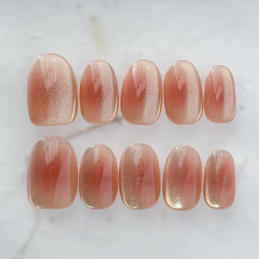 Coral peach cat-eye press-on nails with a soft gold shimmer gradient. Short oval luxury reusable press-on