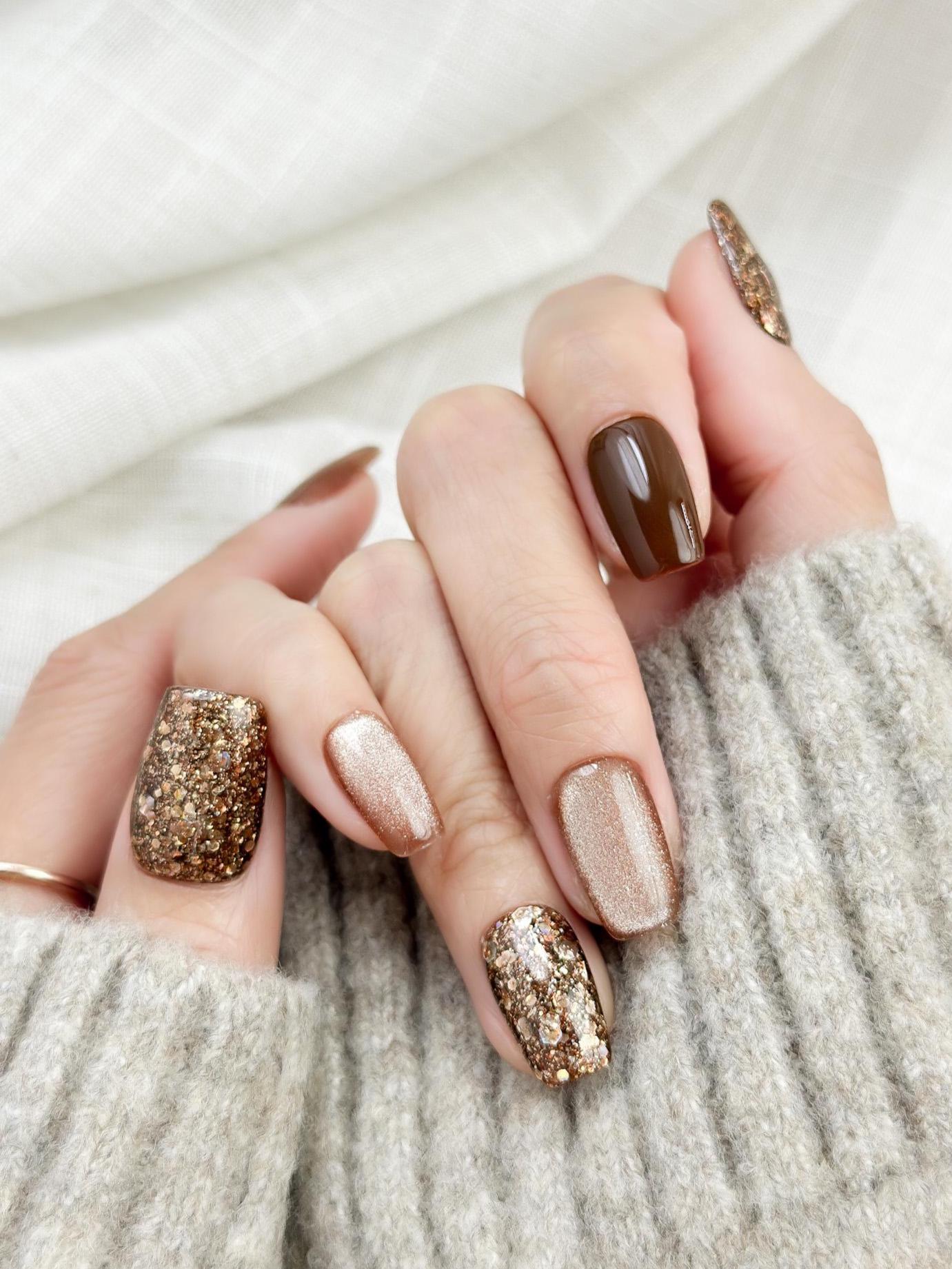 Hand with Brown and gold press-on nails with glossy chocolate brown polish, champagne shimmer, and gold glitter accent nails