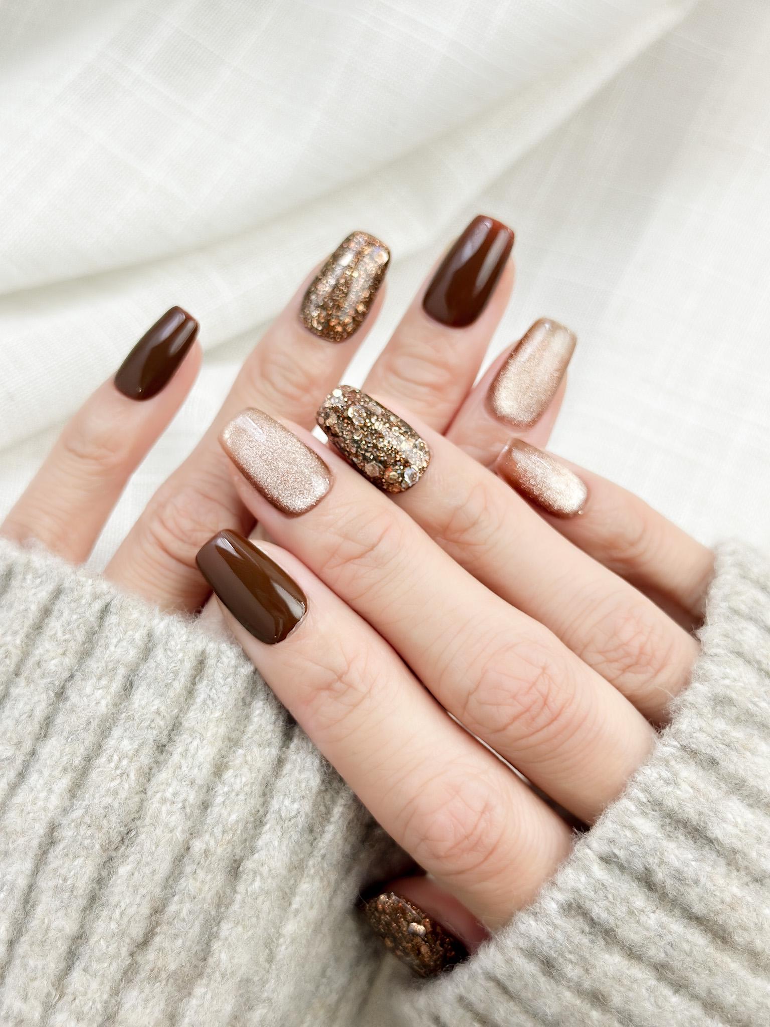 Hand with Brown and gold press-on nails with glossy chocolate brown polish, champagne shimmer, and gold glitter accent nails