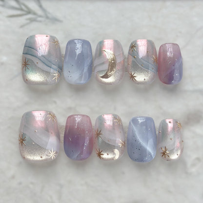 Pastel celestial press-on nails with pink, lavender, and blue marble swirls, gold star accents, and a gold crescent moon design