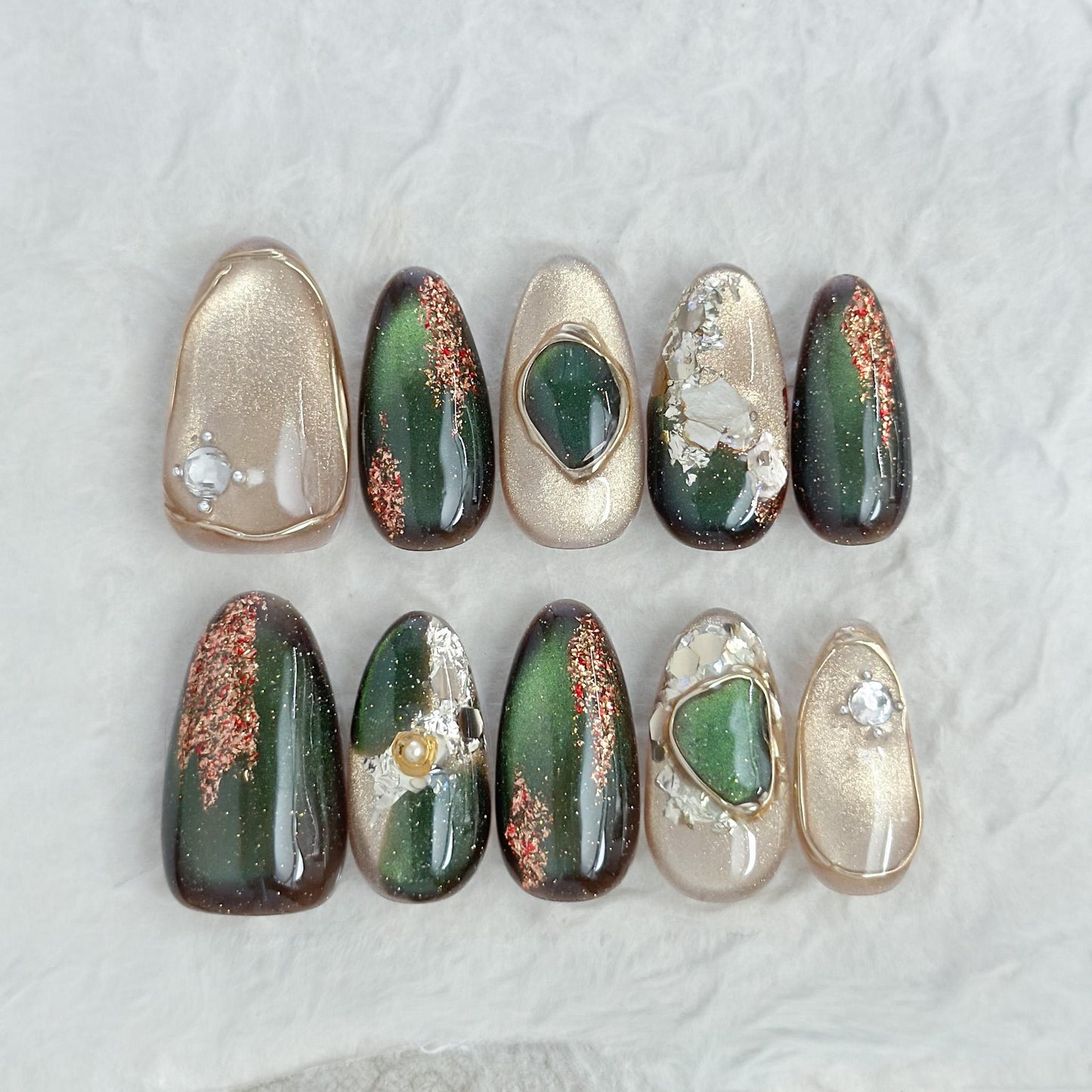 Green and gold gemstone-inspired press-on nails with cat-eye shimmer, glitter accents, gold foil detailing, and 3D crystal embellishments