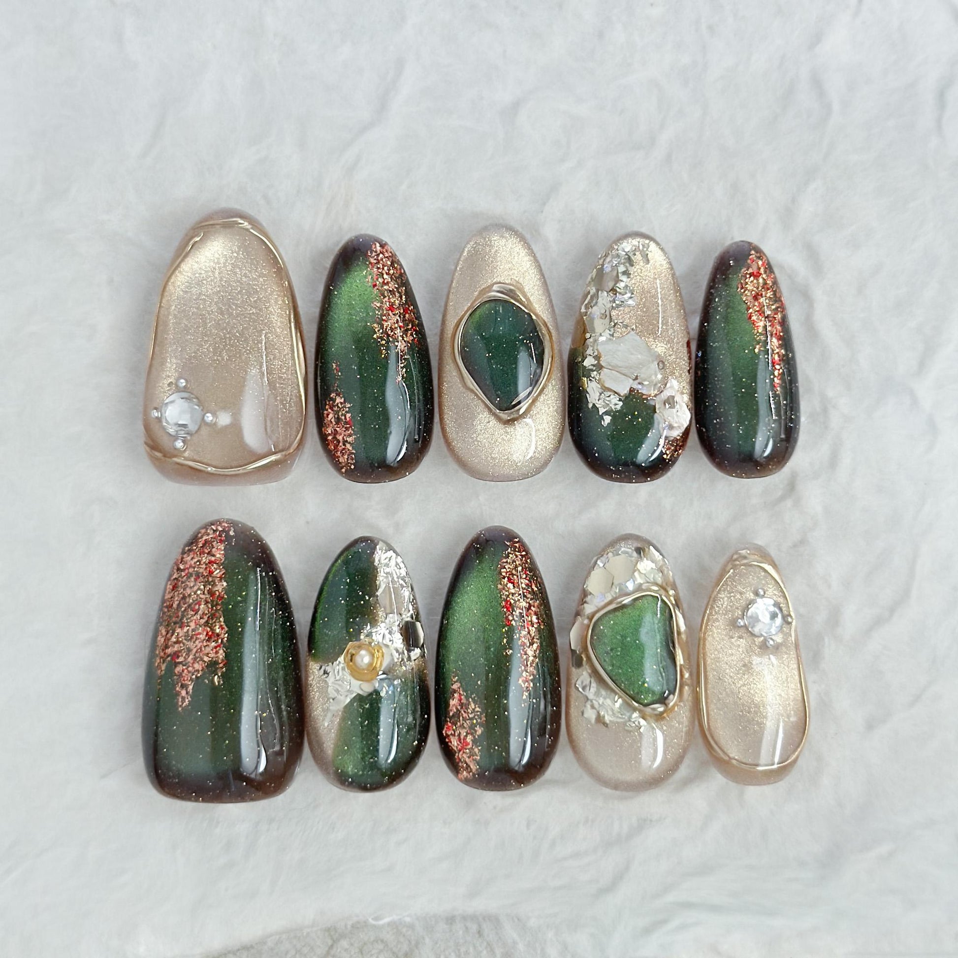 Green and gold gemstone-inspired press-on nails with cat-eye shimmer, glitter accents, gold foil detailing, and 3D crystal embellishments