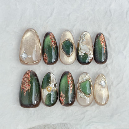 Green and gold gemstone-inspired press-on nails with cat-eye shimmer, glitter accents, gold foil detailing, and 3D crystal embellishments