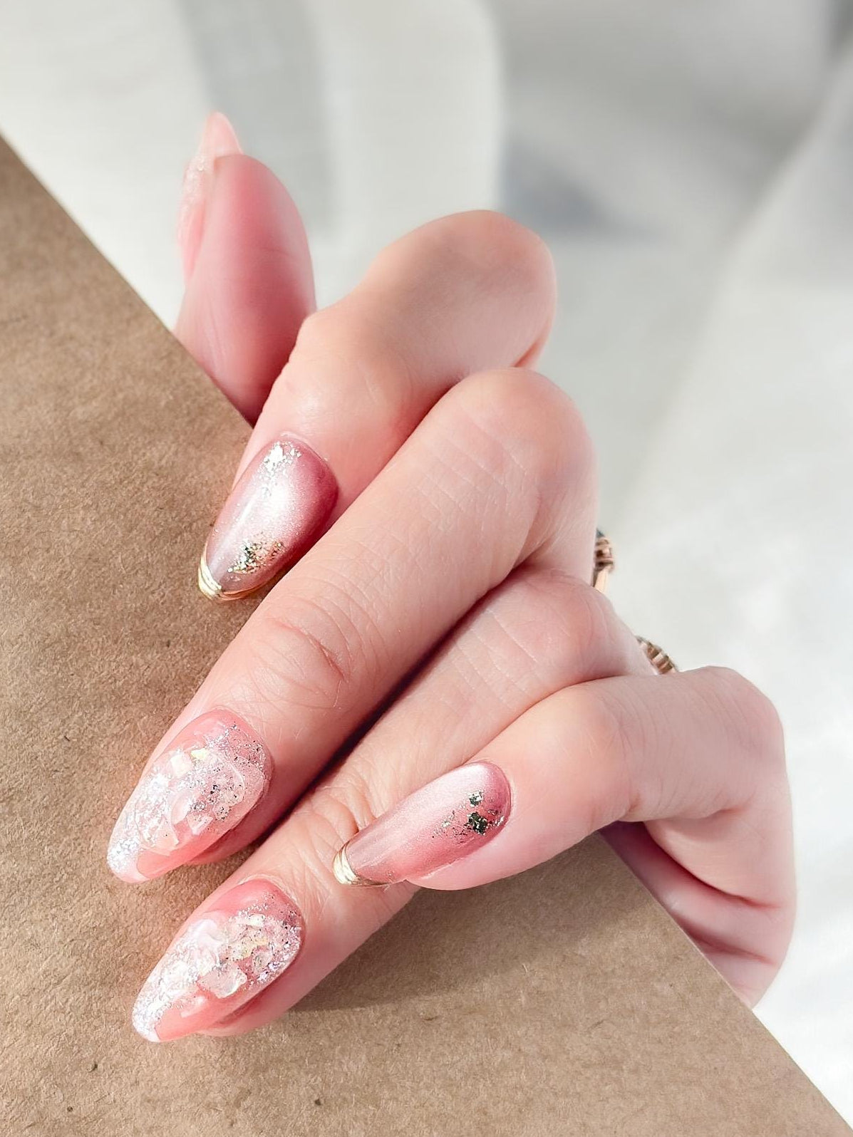 Hand with Pink shimmer press-on nails with iridescent glitter, marble swirl accents, and gold foil details