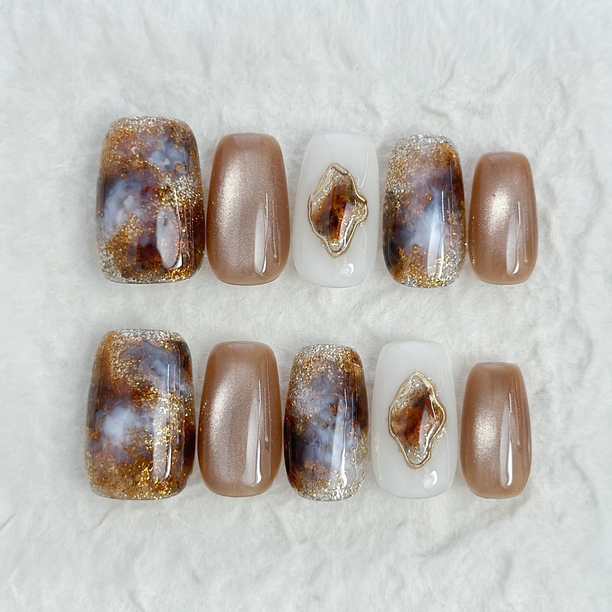 Brown and ivory press-on nails in tortoise pattern, with gold foil detailing, and glossy cat-eye shimmer