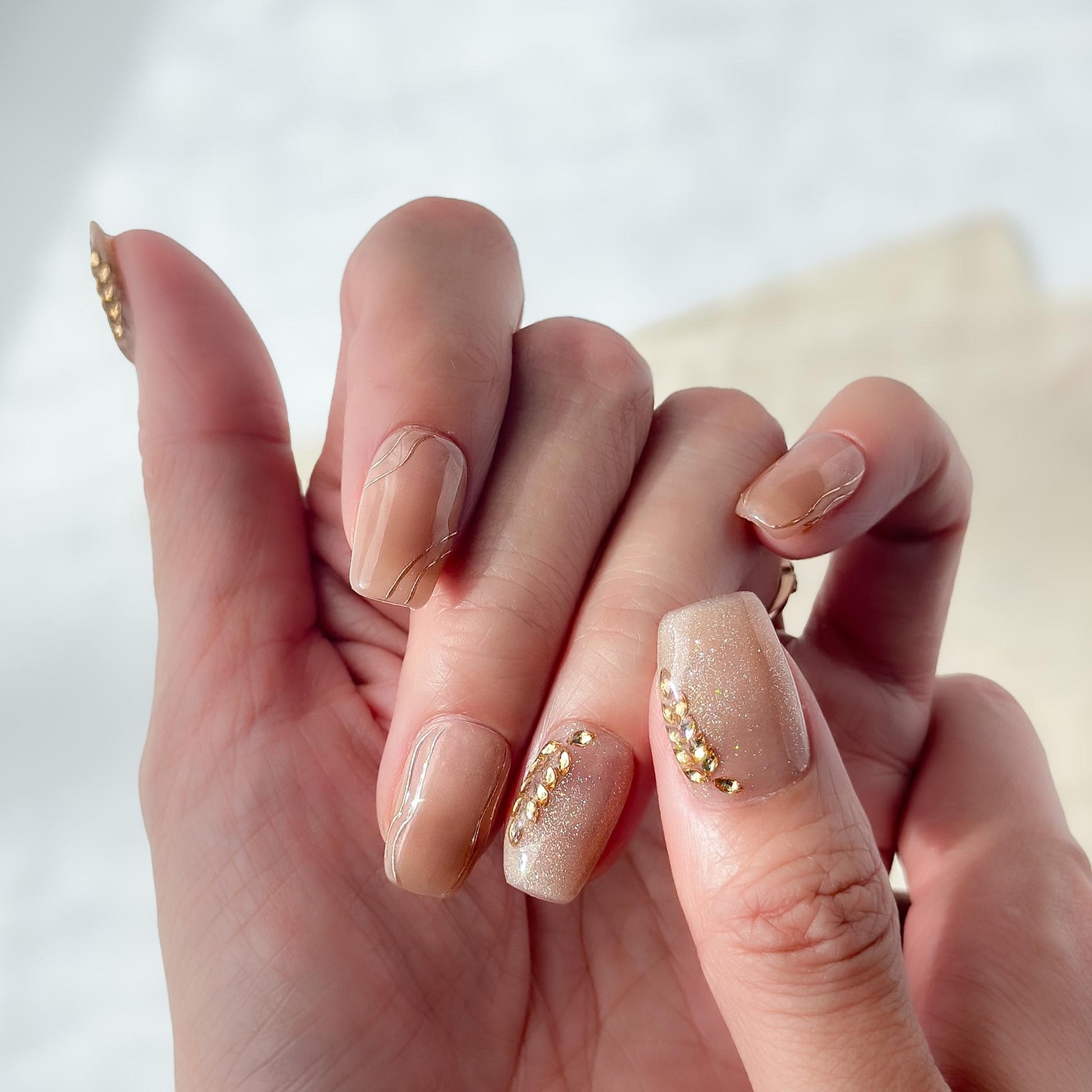 Hand with Nude beige press-on nails with gold leaf accents and glossy marble lines. Elegant neutral nail set with gold embellishments