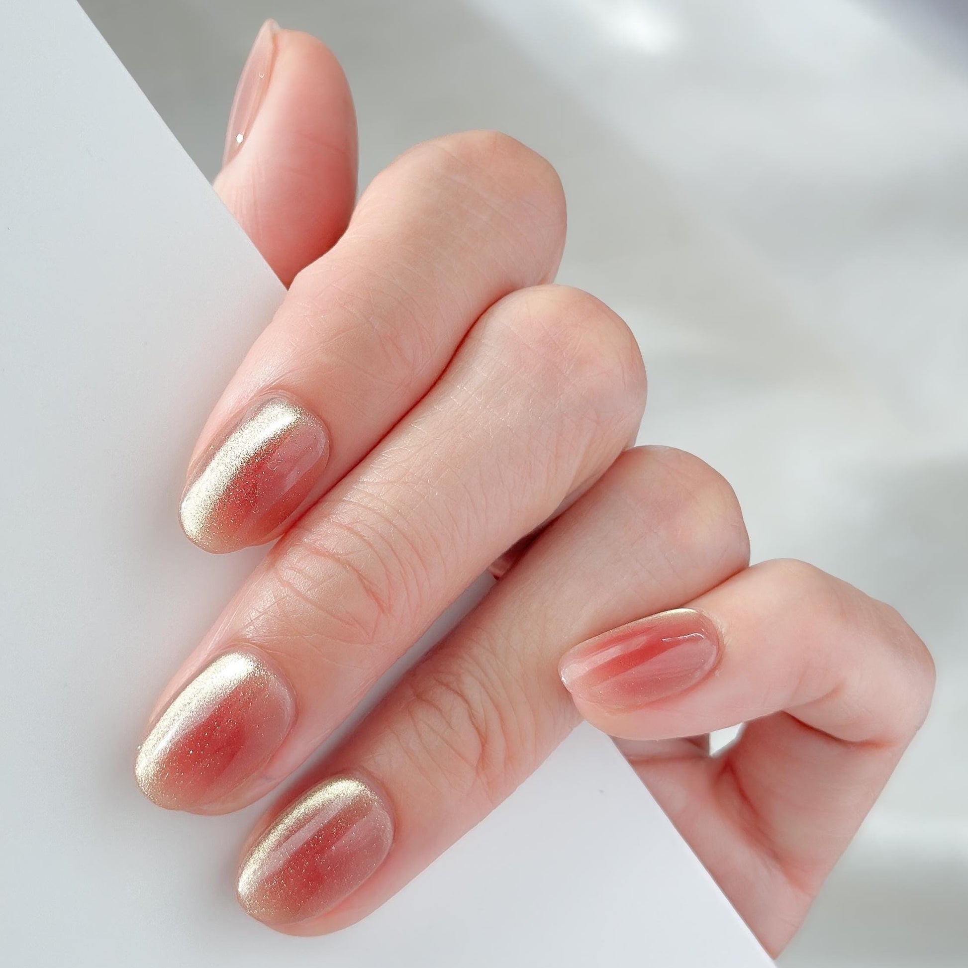 Hand with short Coral peach cat-eye press-on nails with a soft gold shimmer gradient. Short oval luxury reusable press-on