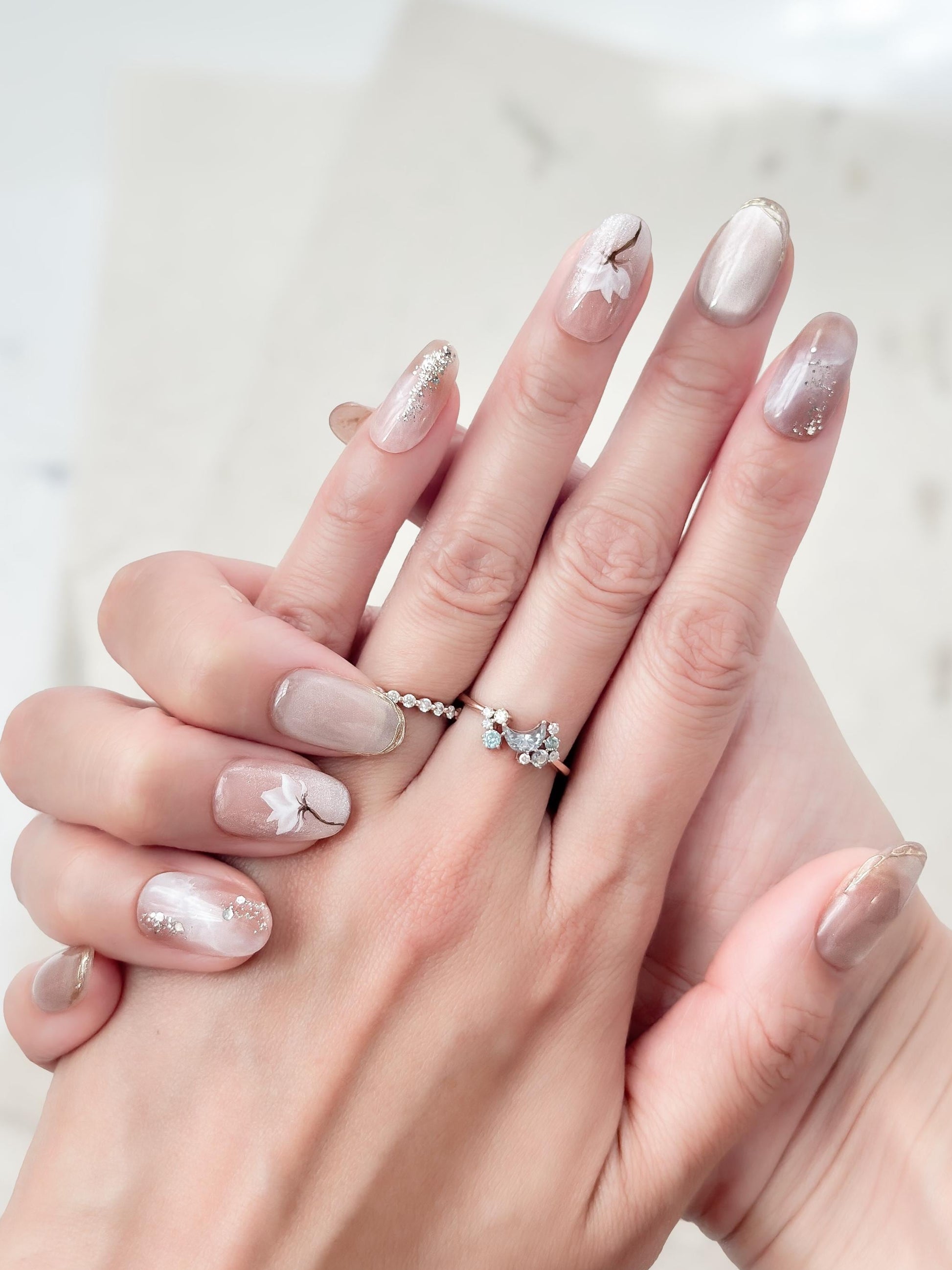 Hand with Pink and pearl white press-on nails with soft marble accents, hand-painted white floral art, silver glitter details, and glossy finish