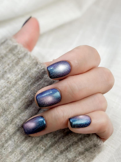 Hand with Short square shaped cat-eye press-on nails in shifting blue, purple, and teal galaxy shimmer