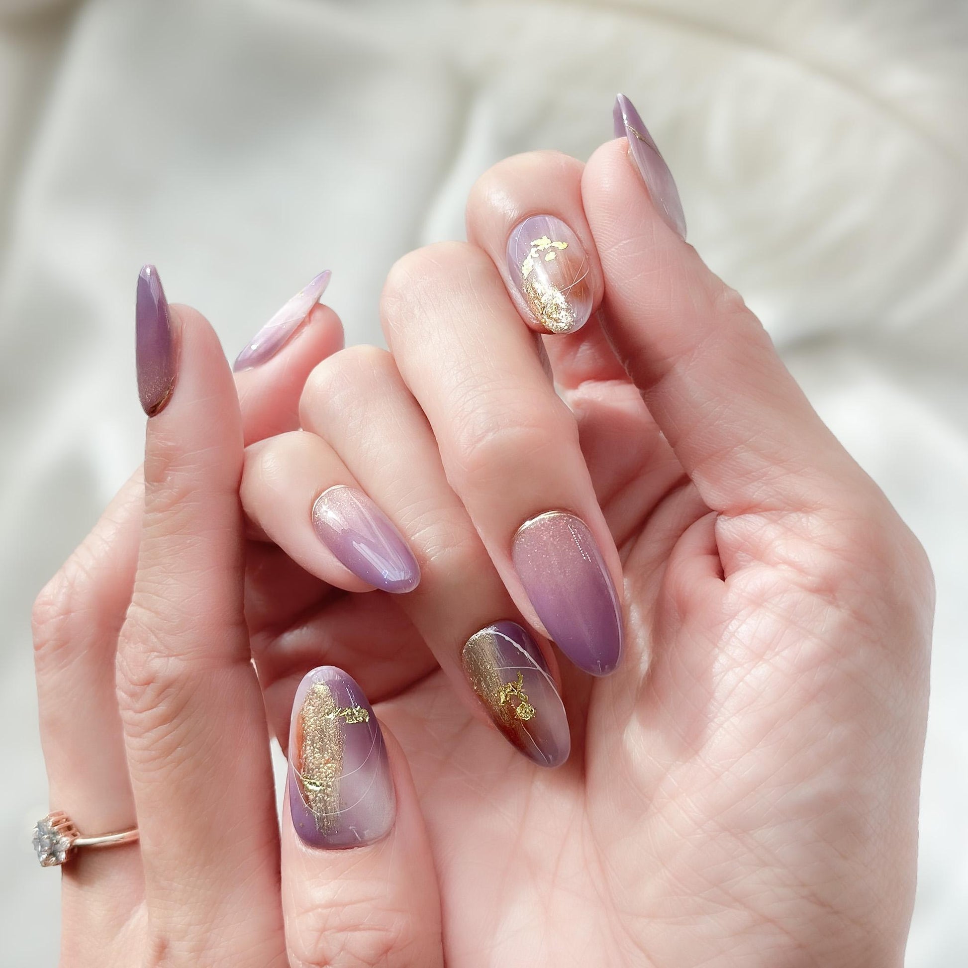 Almond shape purple press-on nails with gold foil accents and soft gradient shimmer. Elegant reusable salon-style press on nails by ManiFleur, featuring lavender ombré, metallic details, and glossy finish