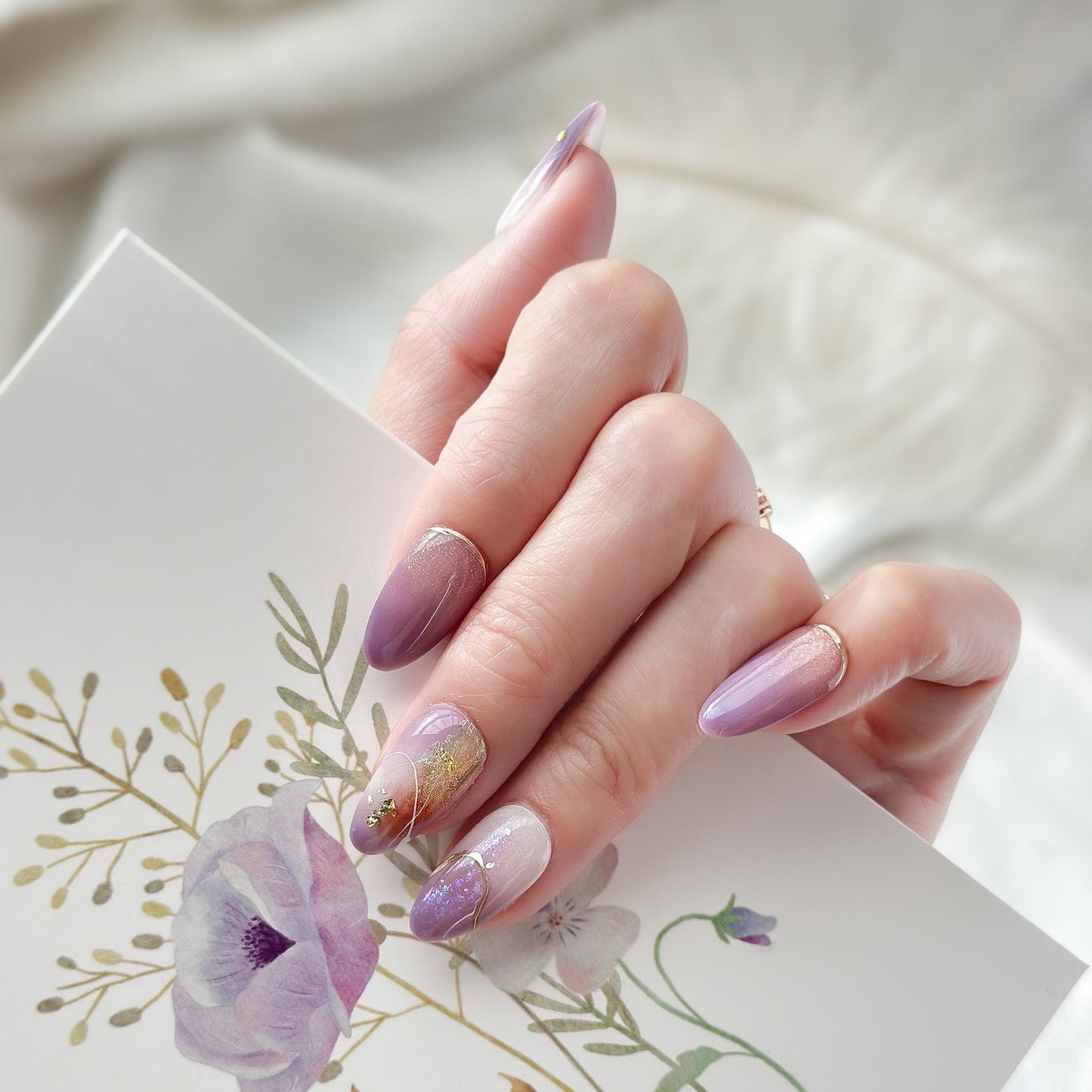 Almond shape purple press-on nails with gold foil accents and soft gradient shimmer. Elegant reusable salon-style press on nails by ManiFleur, featuring lavender ombré, metallic details, and glossy finish