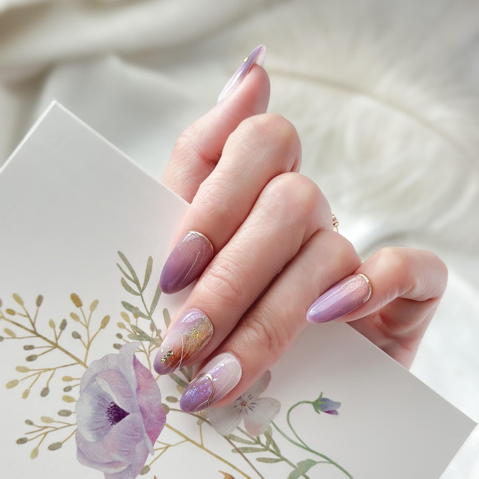 Almond shape purple press-on nails with gold foil accents and soft gradient shimmer. Elegant reusable salon-style press on nails by ManiFleur, featuring lavender ombré, metallic details, and glossy finish