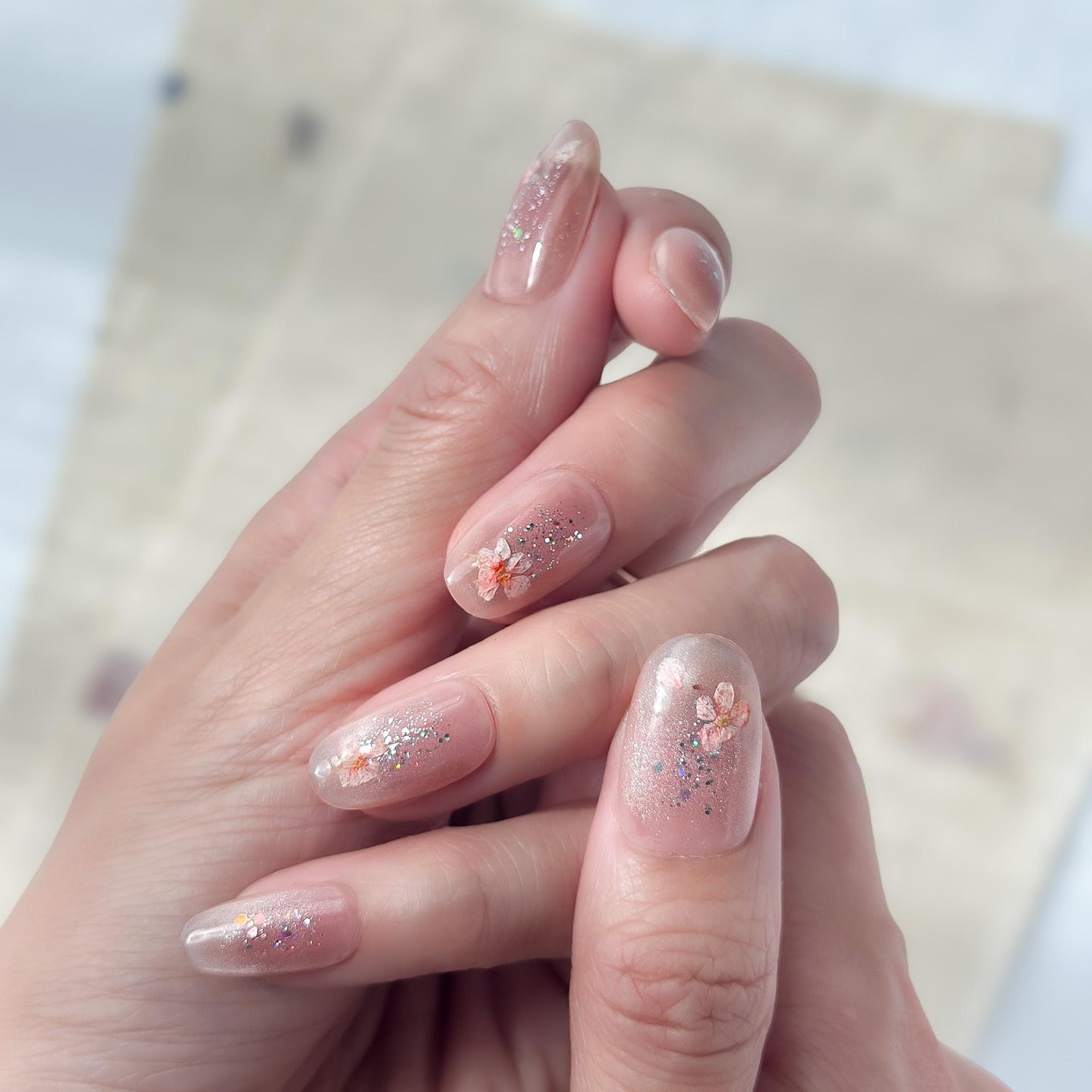 Hand with press on nail made with real dried flowers encased in a translucent blush base with fine glitter