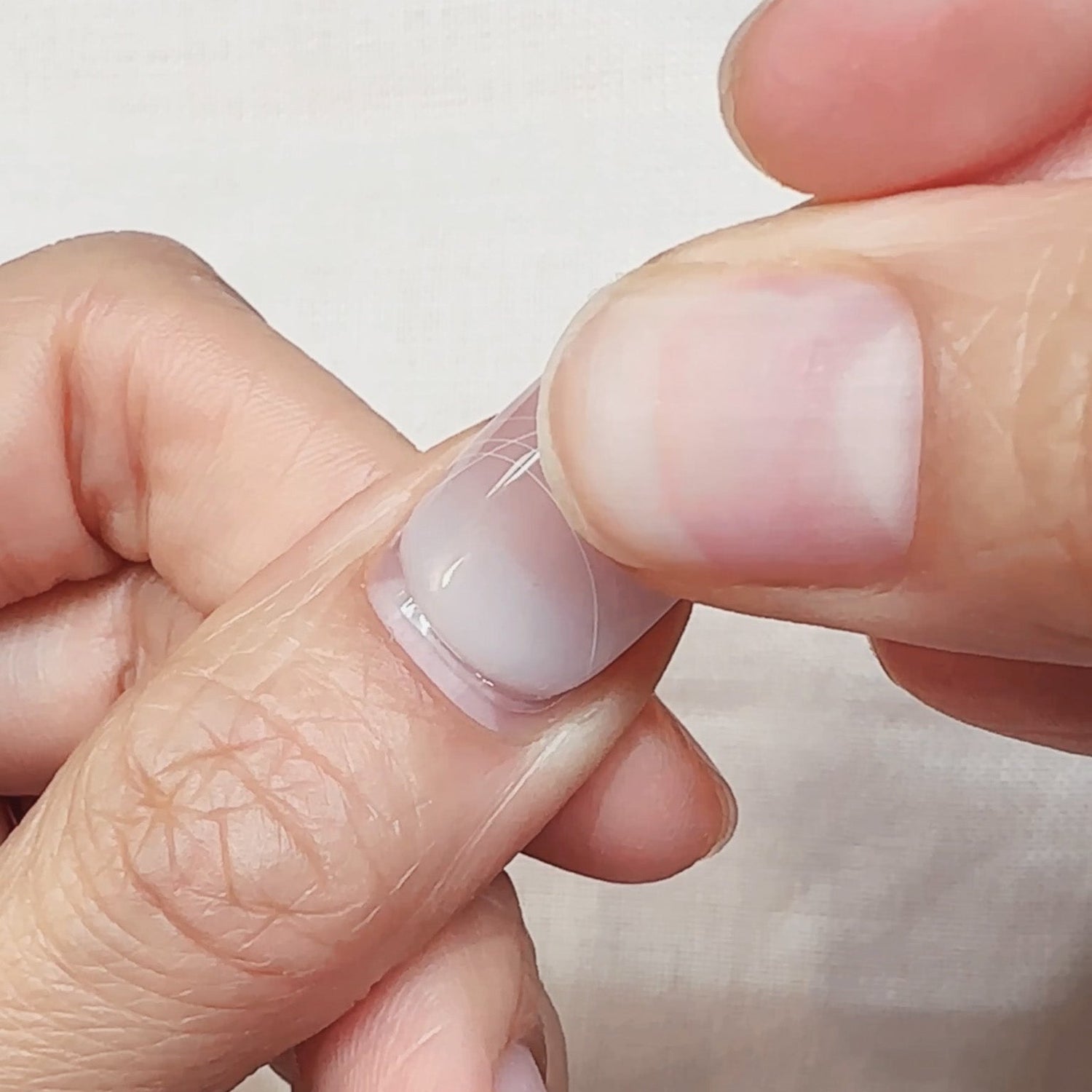 Close-up of a hand with a clear nail polish on a plain background