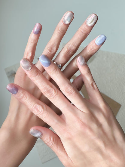 Hand with Pastel celestial press-on nails with pink, lavender, and blue marble swirls, gold star accents, and a gold crescent moon design