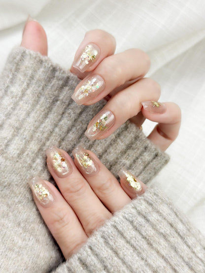 Hand showing press on nail with nude base and crushed foil glitter accent in gold, artificial nails