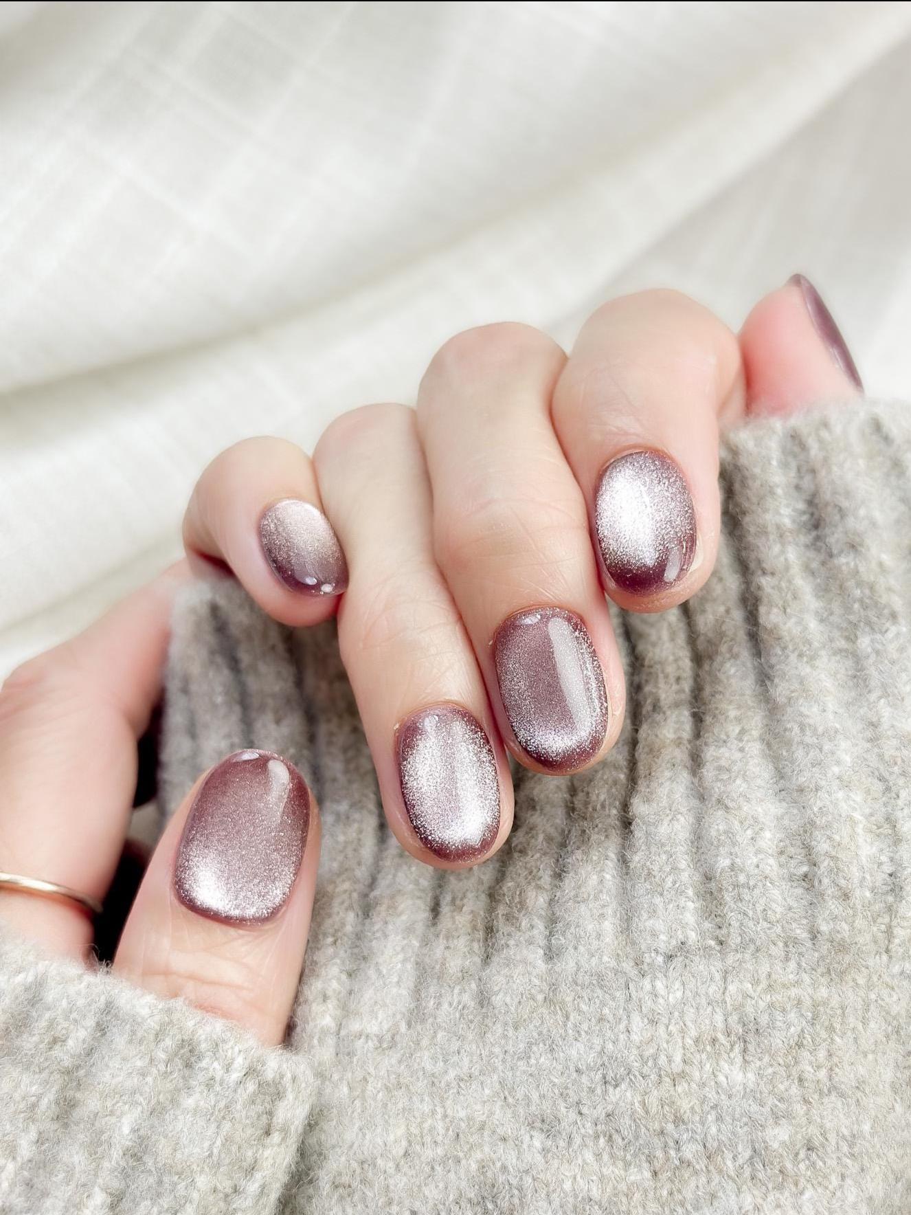 Short oval press-on nails in a metallic mauve cat-eye shimmer, glossy finish, luxury reusable press-on manicure by ManiFleur. Elegant mauve shimmer nails styled against a cozy knit sweater