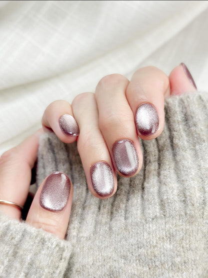 Short oval press-on nails in a metallic mauve cat-eye shimmer, glossy finish, luxury reusable press-on manicure by ManiFleur. Elegant mauve shimmer nails styled against a cozy knit sweater