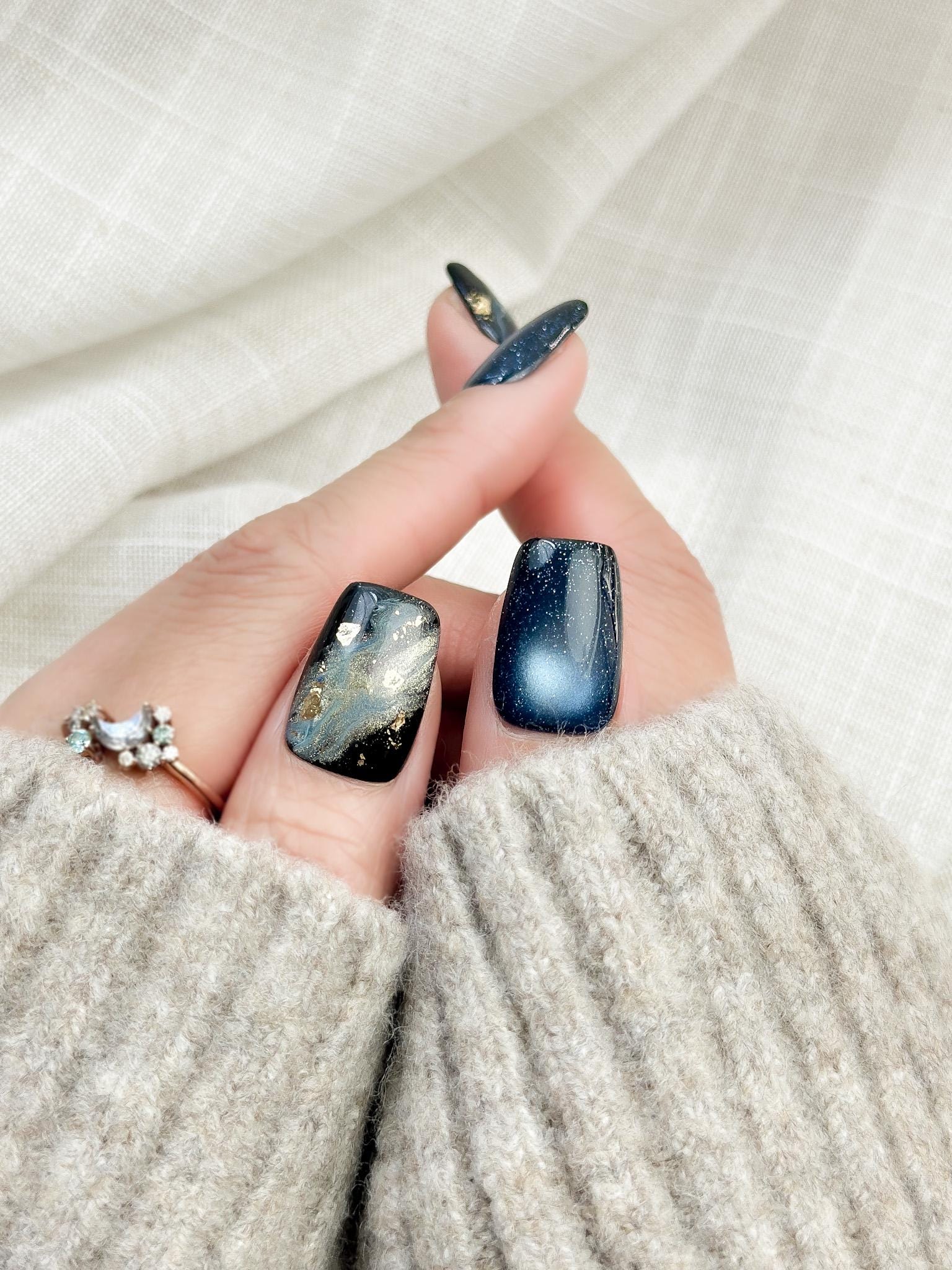 Hand with blue cat-eye press-on nails with galaxy shimmer and abstract marble accents in green, gold, and silver foil
