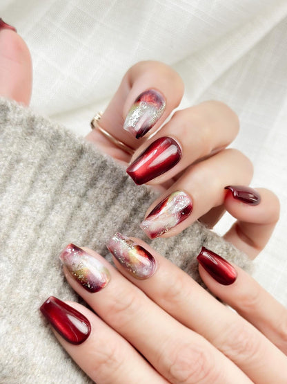 close up of hand with press-on nails in deep burgundy red with multi-color abstract art accents marble effect and silver glitter details, festive holiday color