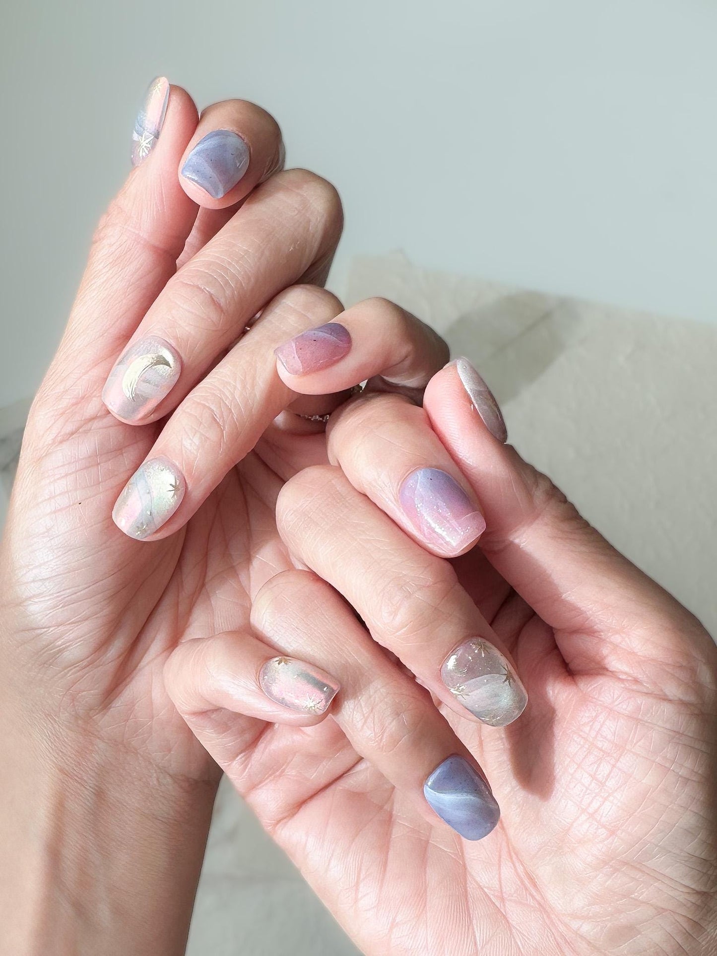 Hand with Pastel celestial press-on nails with pink, lavender, and blue marble swirls, gold star accents, and a gold crescent moon design