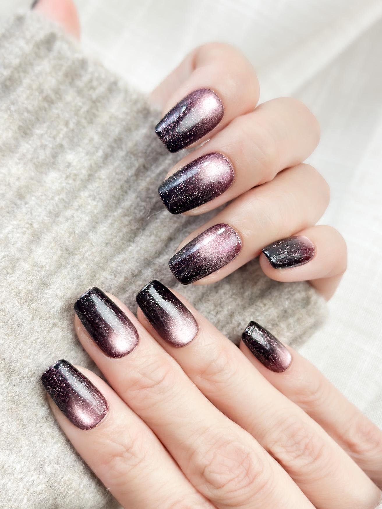 Hand with Short square press-on nails in a deep plum purple cat-eye shimmer with black gradient edges and silver sparkle accents