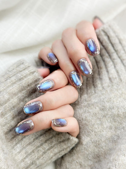 Hand with Square shaped grey-blue cat eye press-on nails with metallic shimmer and gold foil border accents