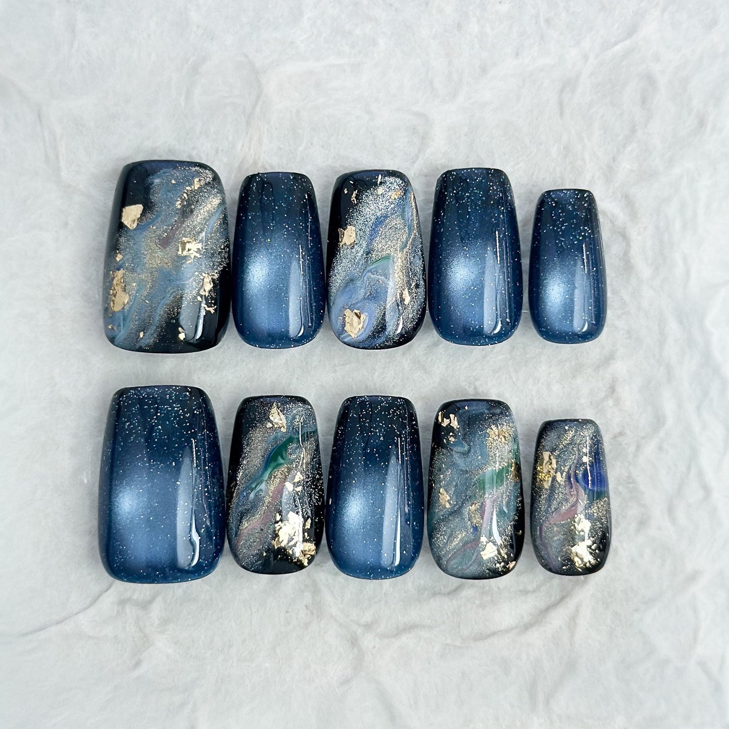 Luxury blue cat-eye press-on nails with galaxy shimmer and abstract marble accents in green, gold, and silver foil