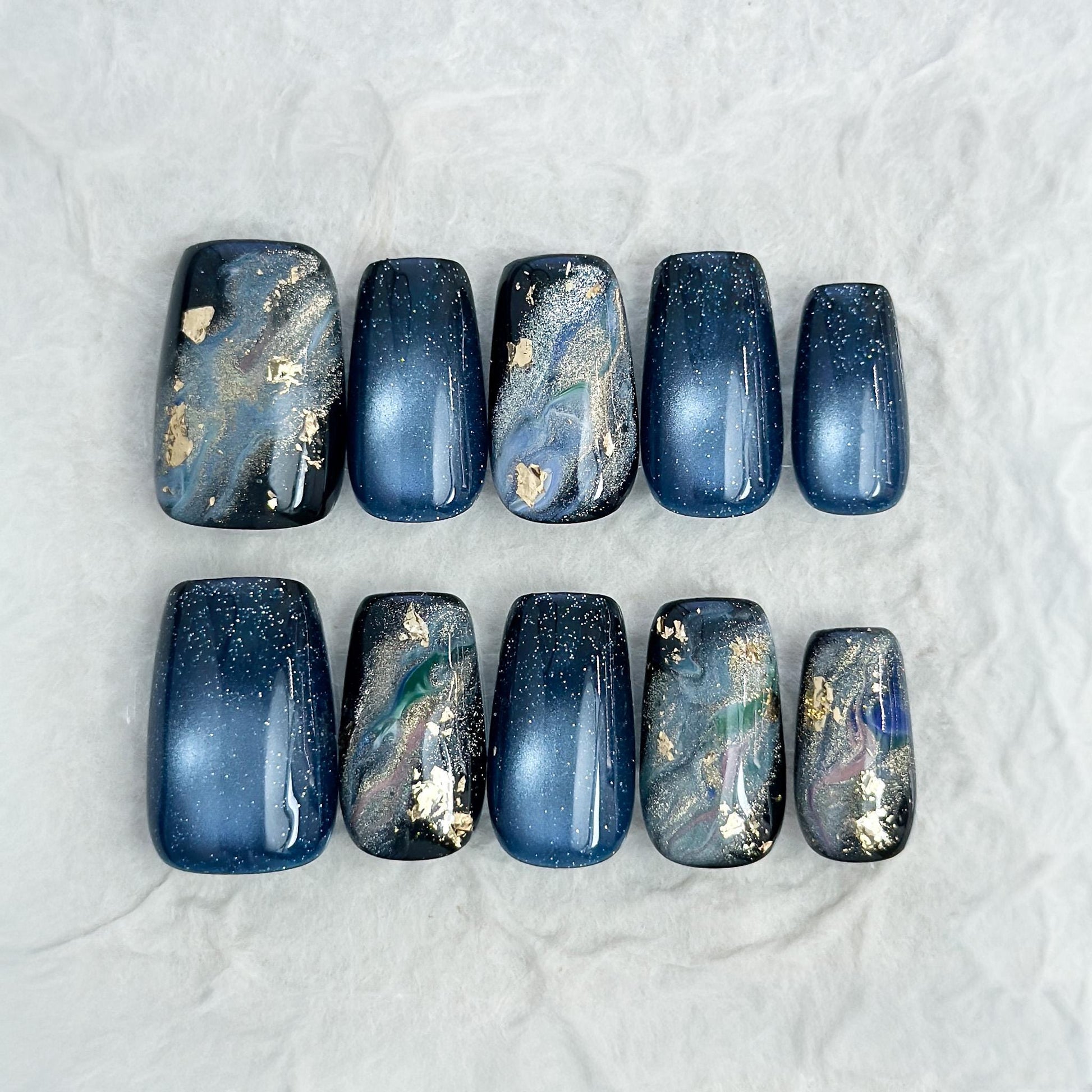 Luxury blue cat-eye press-on nails with galaxy shimmer and abstract marble accents in green, gold, and silver foil