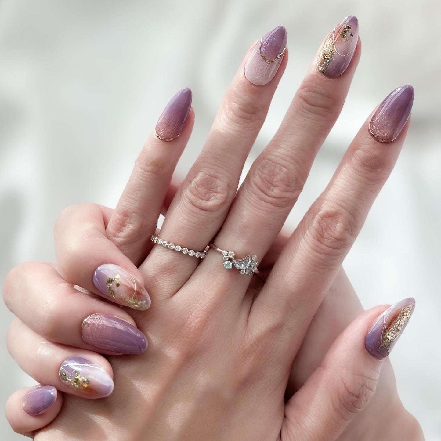 Hand with almond shape purple press-on nails with gold foil accents and soft gradient shimmer. Elegant reusable salon-style press on nails by ManiFleur, featuring lavender ombré, metallic details, and glossy finish