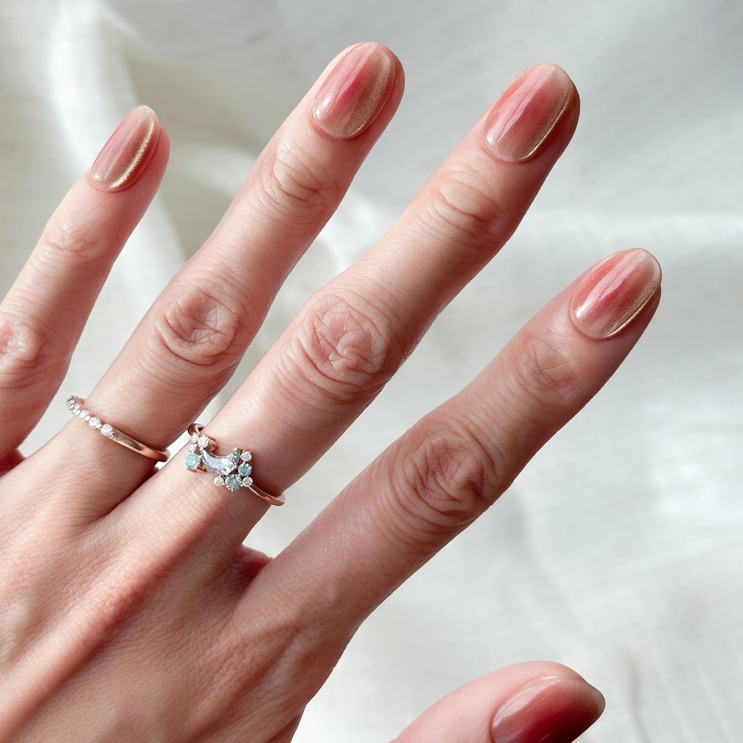 Hand with short Coral peach cat-eye press-on nails with a soft gold shimmer gradient. Short oval luxury reusable press-on