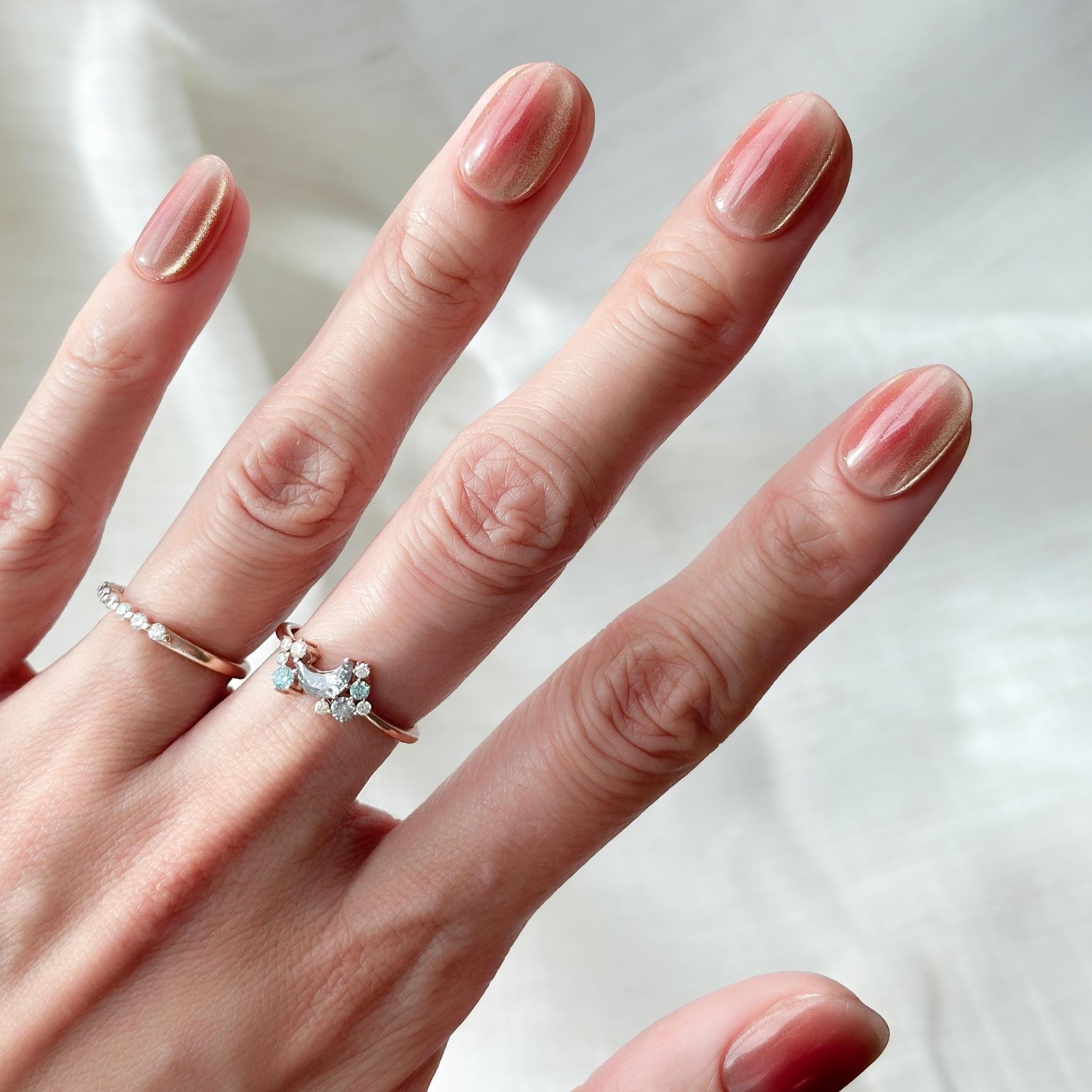 Hand with short Coral peach cat-eye press-on nails with a soft gold shimmer gradient. Short oval luxury reusable press-on