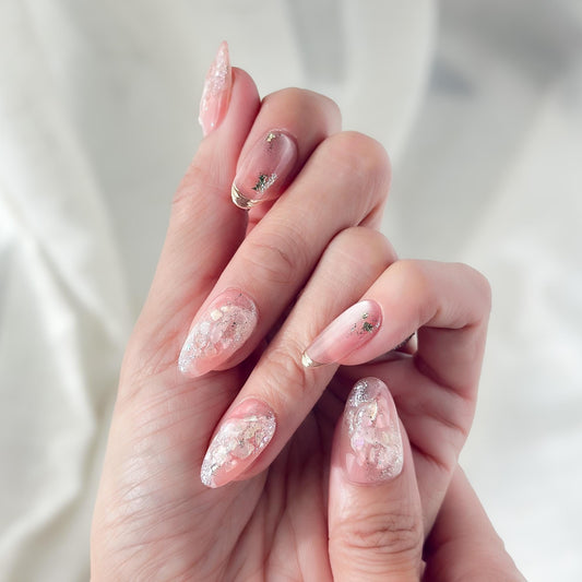 Hand with Pink shimmer press-on nails with iridescent glitter, marble swirl accents, and gold foil details