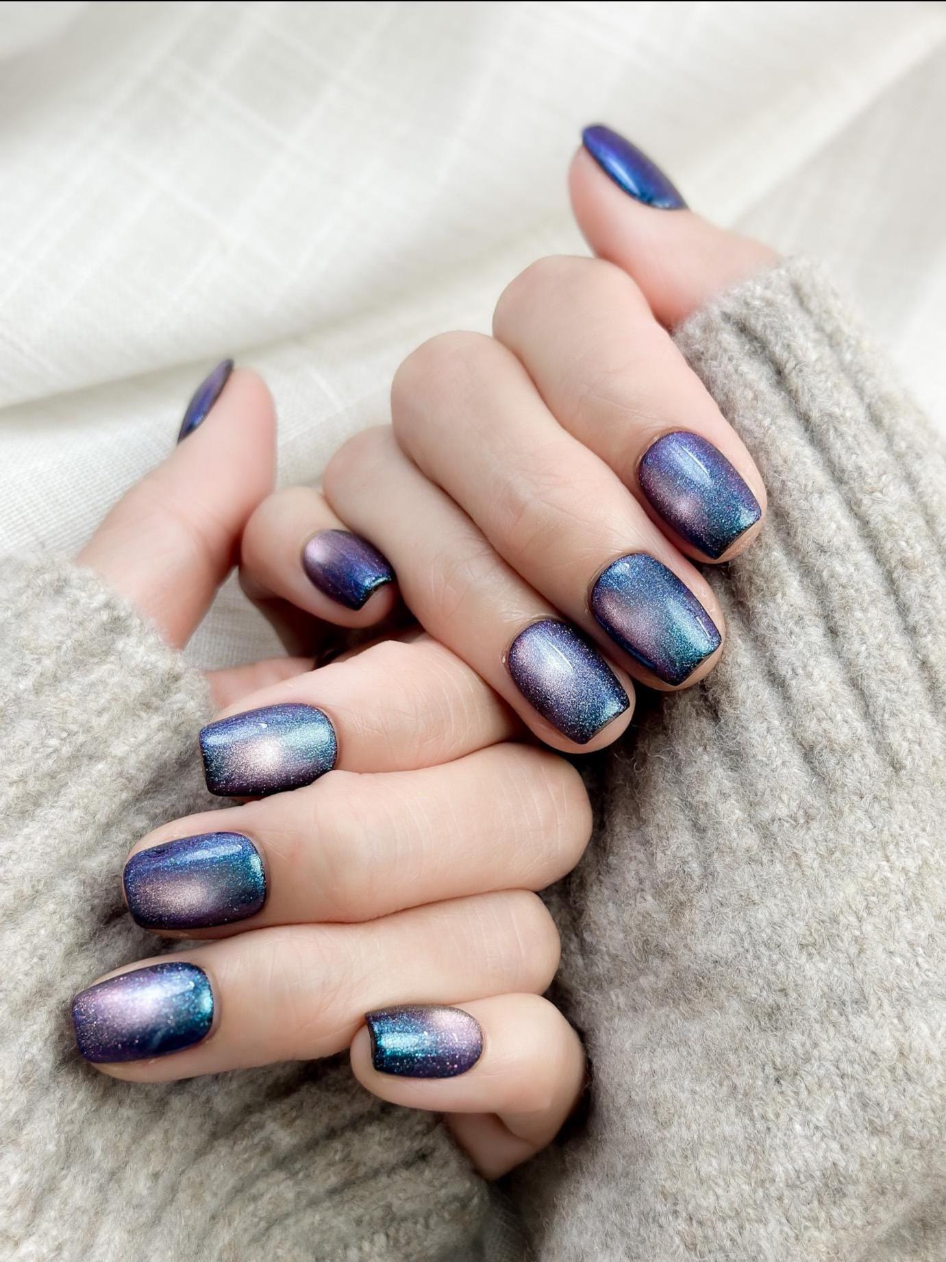 Hand with Short square shaped cat-eye press-on nails in shifting blue, purple, and teal galaxy shimmer