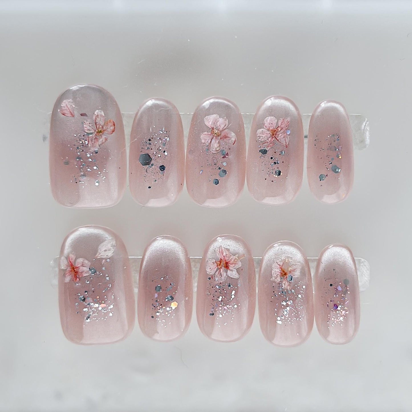 Press on nail made with real dried flowers encased in a translucent blush base with fine glitter