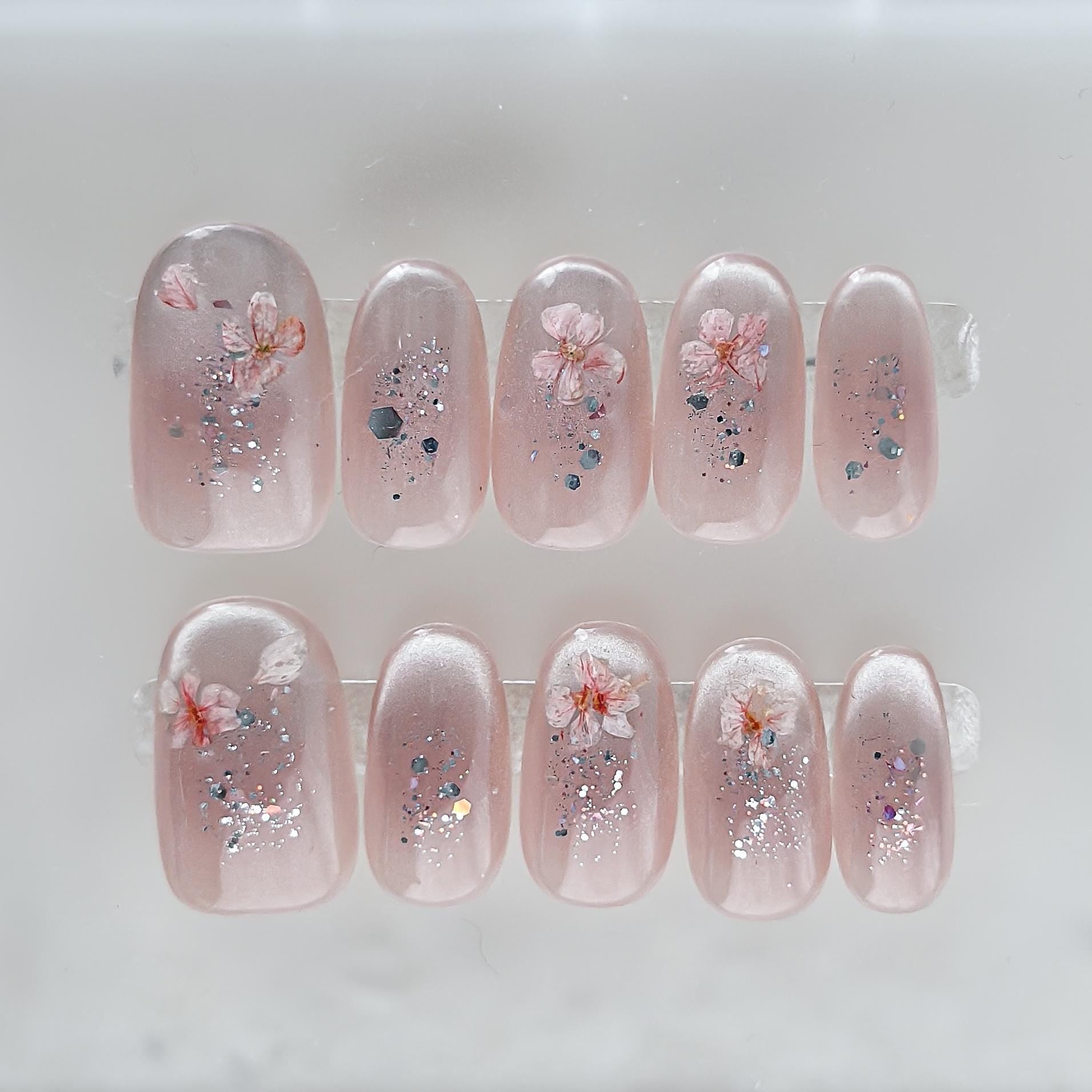 Press on nail made with real dried flowers encased in a translucent blush base with fine glitter