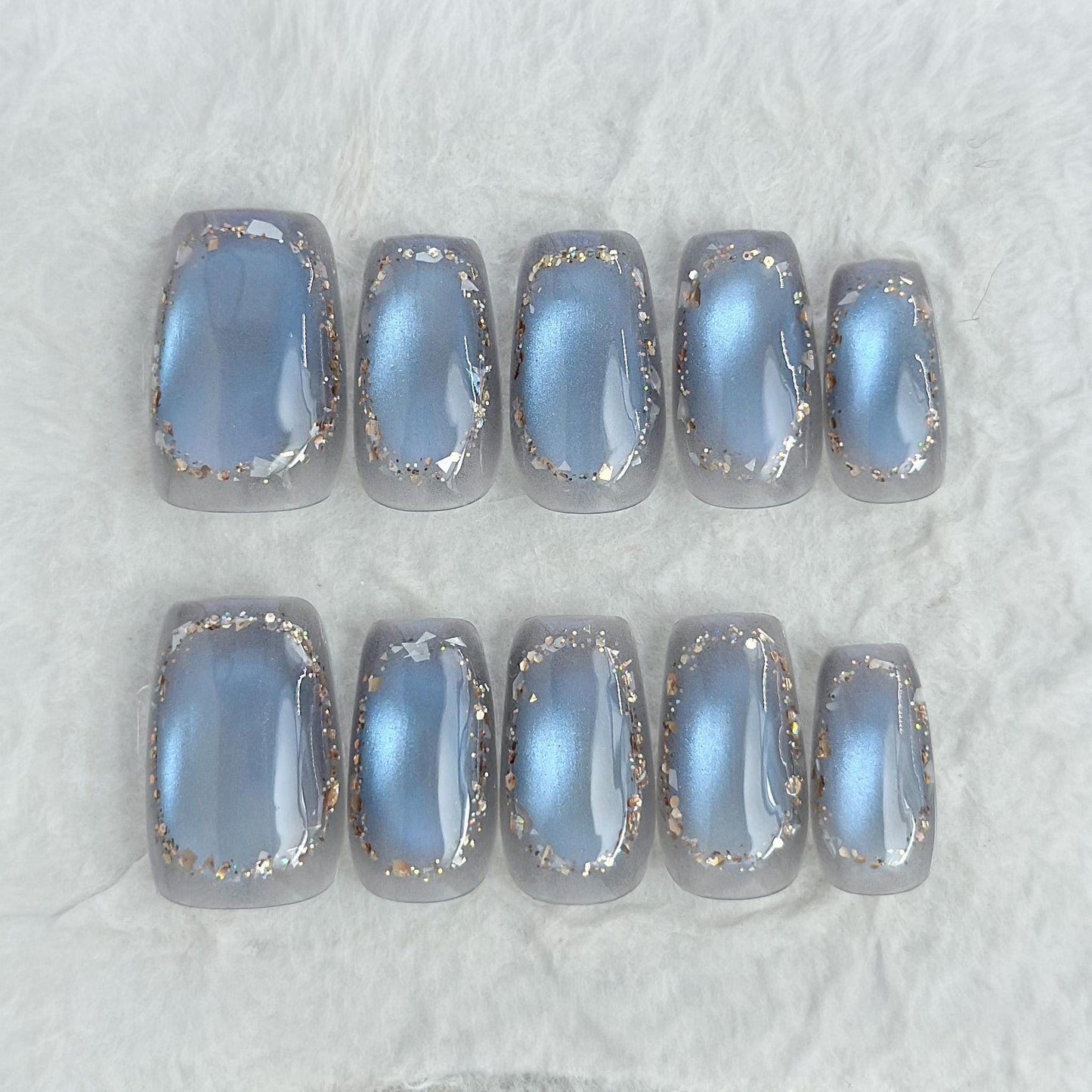 Square shaped grey-blue cat eye press-on nails with metallic shimmer and gold foil border accents