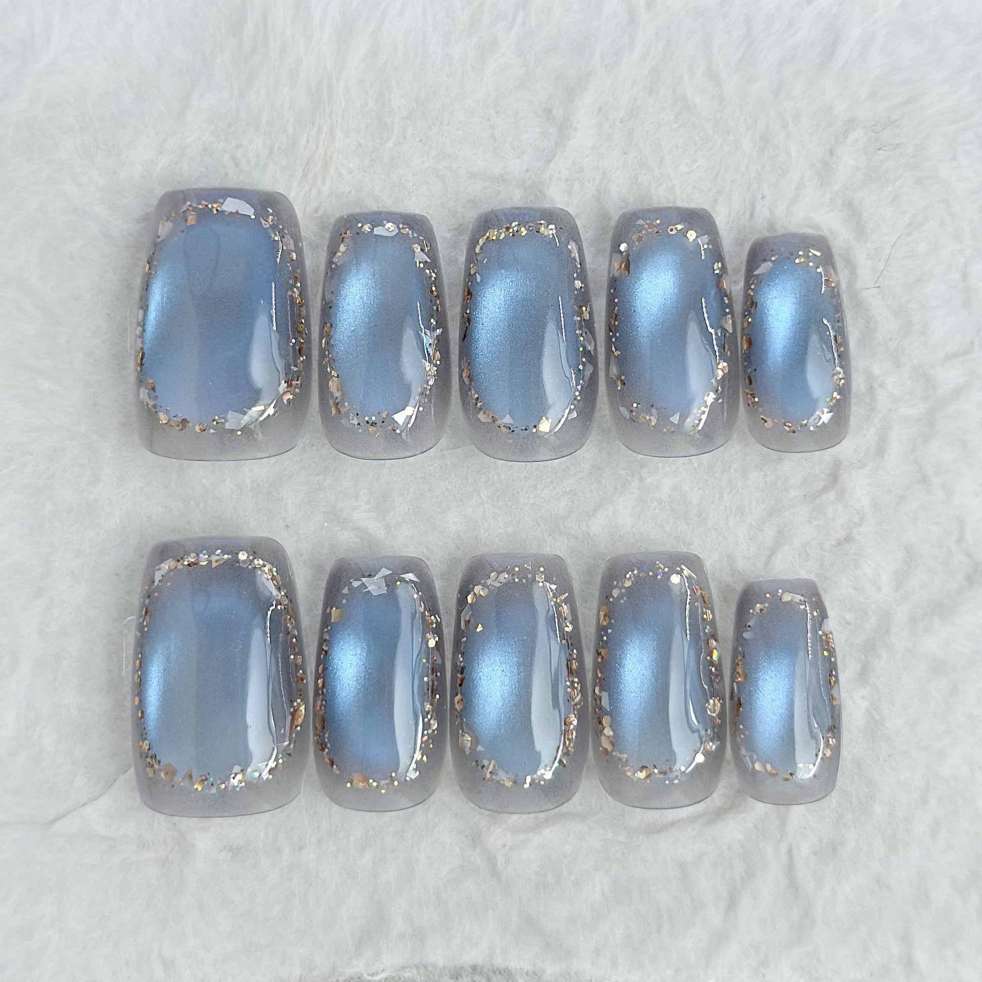 Square shaped grey-blue cat eye press-on nails with metallic shimmer and gold foil border accents