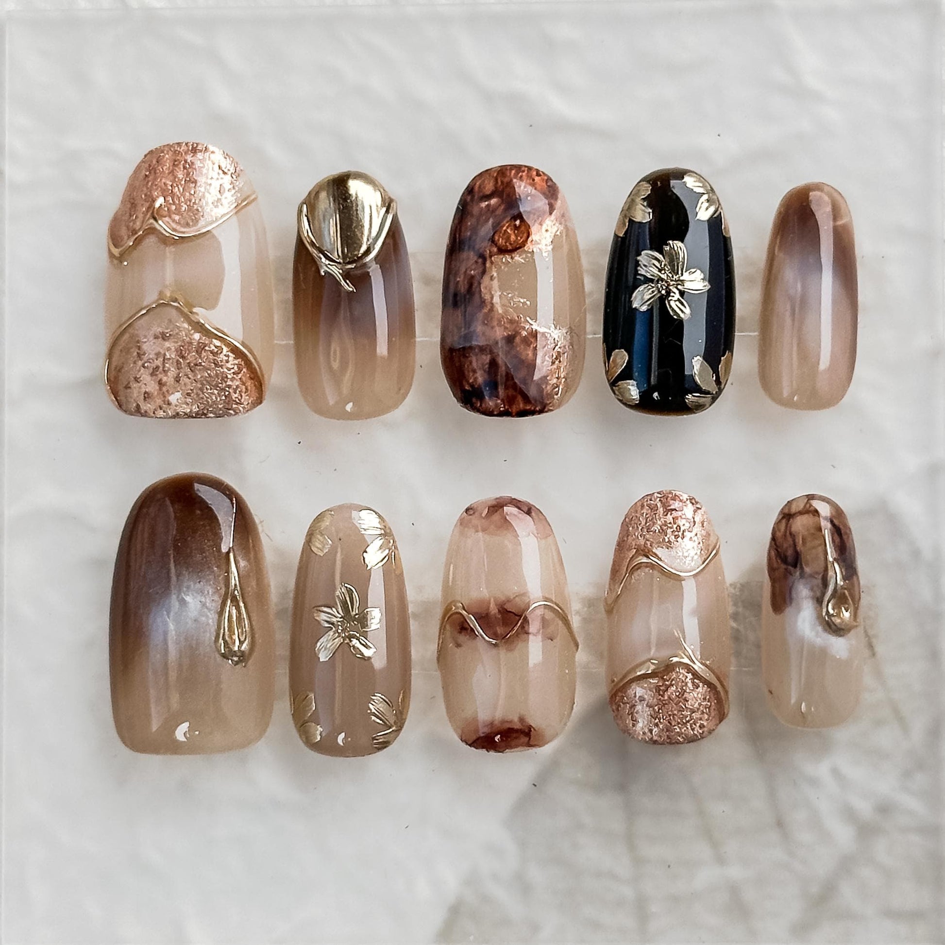 Luxury reusable press-on nails in neutral taupe and mocha tones with gold foil accents, marble detailing, and embossed metallic floral designs