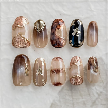 Luxury reusable press-on nails in neutral taupe and mocha tones with gold foil accents, marble detailing, and embossed metallic floral designs