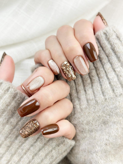 Hand with Brown and gold press-on nails with glossy chocolate brown polish, champagne shimmer, and gold glitter accent nails