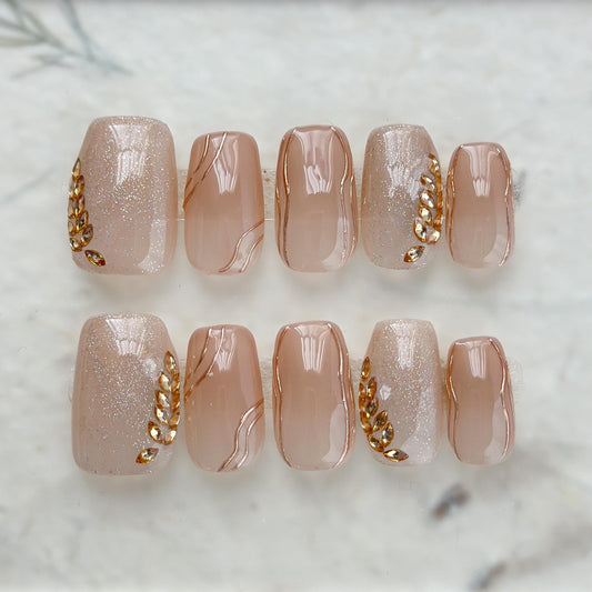 Nude beige press-on nails with gold leaf accents and glossy marble lines. Elegant neutral nail set with gold embellishments