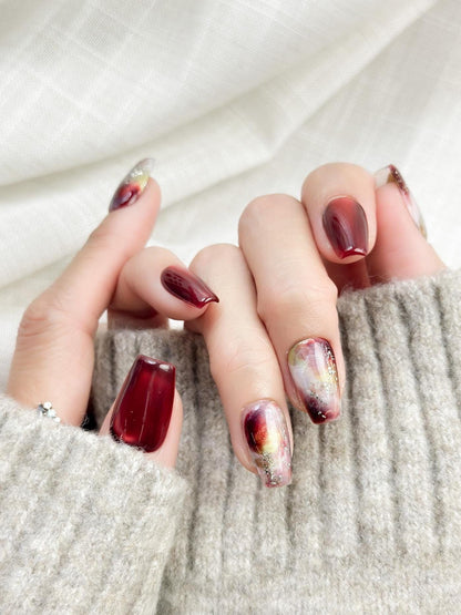 close up of hand with press-on nails in deep burgundy red with multi-color abstract art accents marble effect and silver glitter details, festive holiday color
