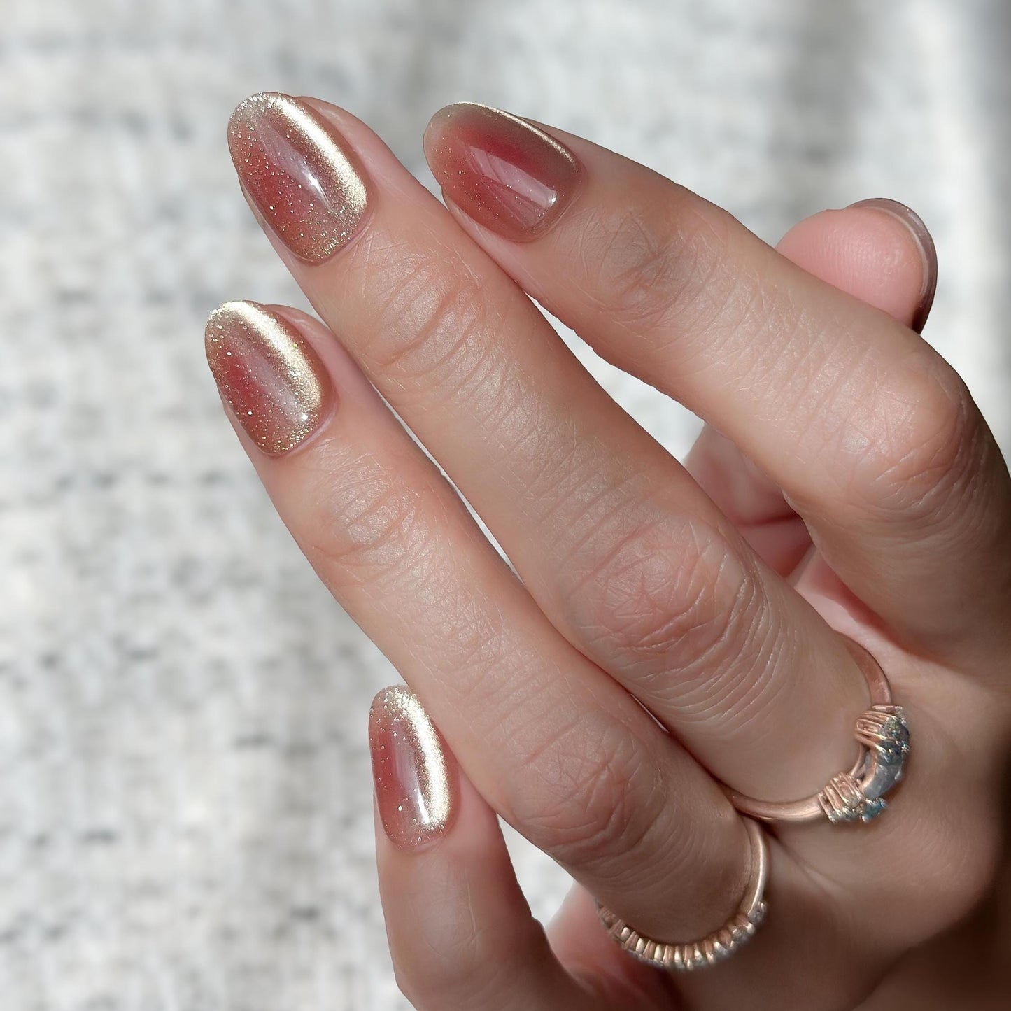 Hand with short Coral peach cat-eye press-on nails with a soft gold shimmer gradient. Short oval luxury reusable press-on