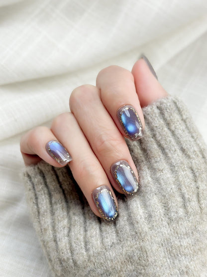 Hand with Square shaped grey-blue cat eye press-on nails with metallic shimmer and gold foil border accents
