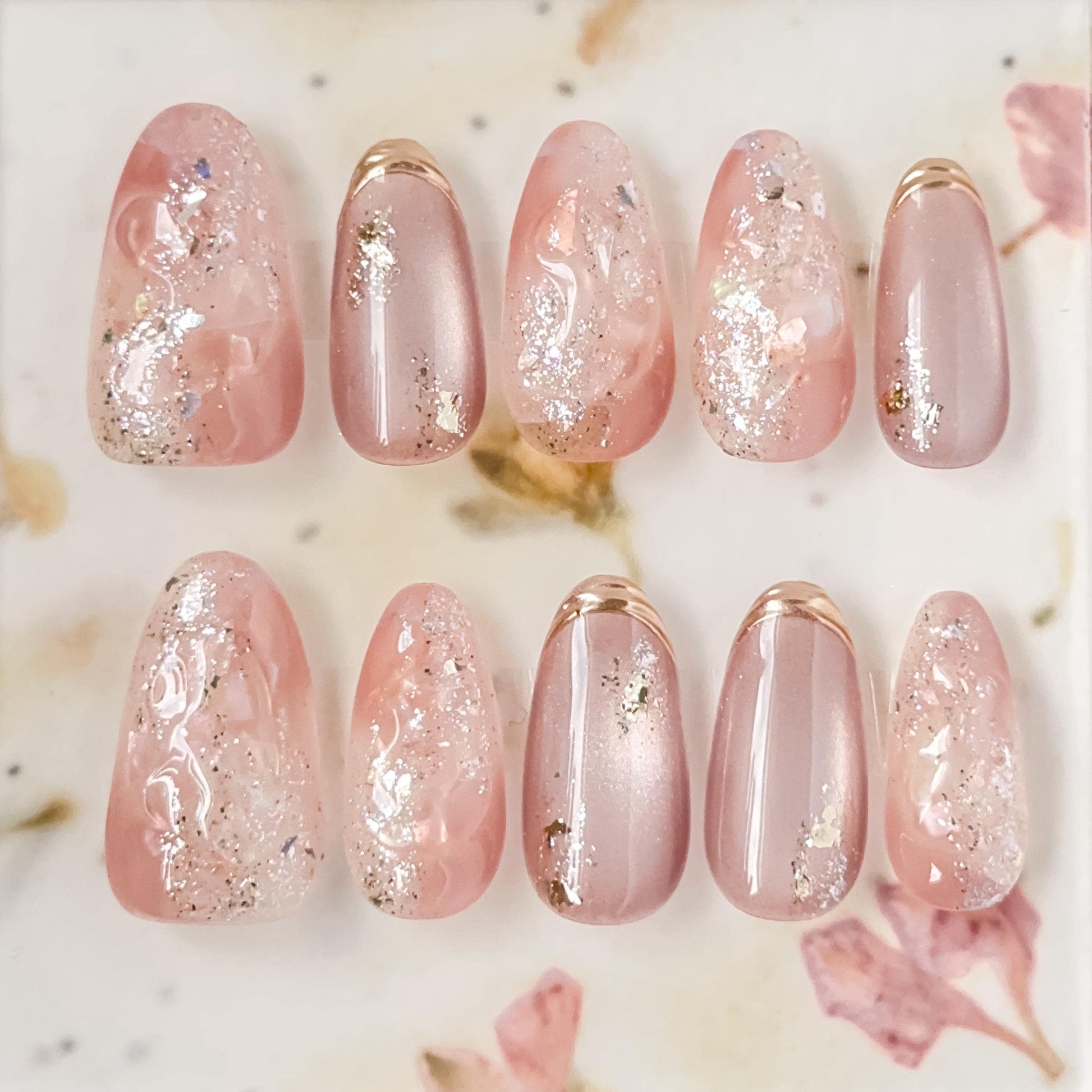 Pink shimmer press-on nails with iridescent glitter, marble swirl accents, and gold foil details