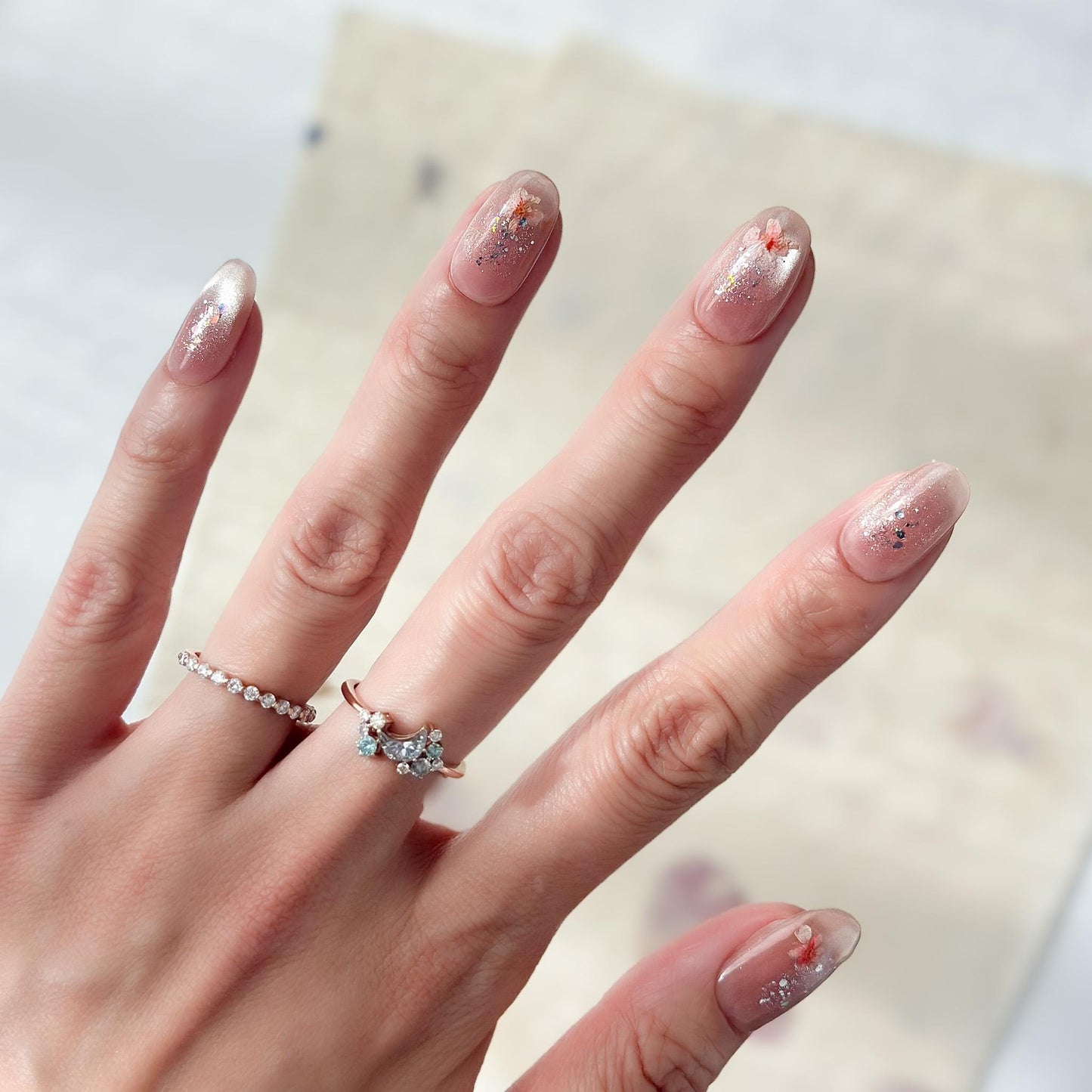 Hand with press on nail made with real dried flowers encased in a translucent blush base with fine glitter